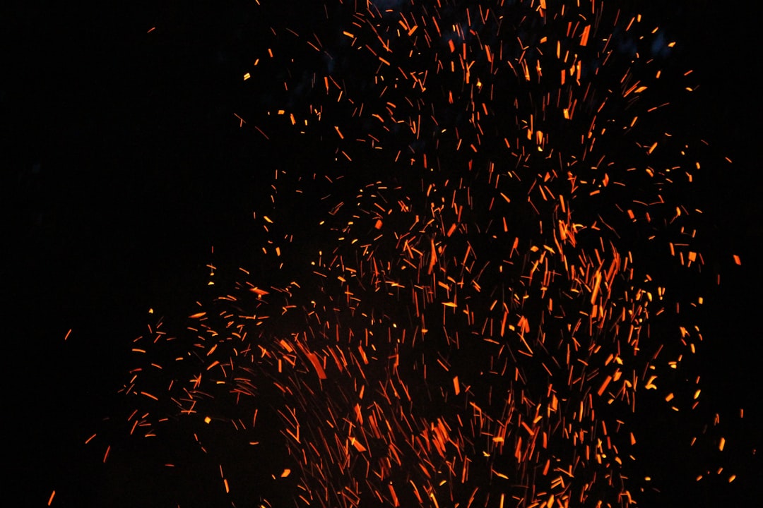Bright orange embers rising into the dark night air from a fire